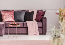 10x hoe je sfeer brengt in je interieur Paarse bank met sierkussens, een kleed, een bijzettafeltje en accesoires
